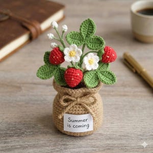 May include: A crocheted strawberry arrangement in a small burlap bag. The arrangement includes red strawberries, white flowers with yellow centers, and green leaves. A small tag reads "Summer is coming".