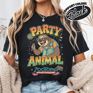 May include: Black t-shirt with a colorful graphic featuring a sloth wearing sunglasses and a Hawaiian shirt, holding a sparkler. Text includes "PARTY ANIMAL ZOOTOPIA BETTER ZOOGETHER" in a retro font. The words "COMFORT COLORS Black" are also printed on the shirt.
