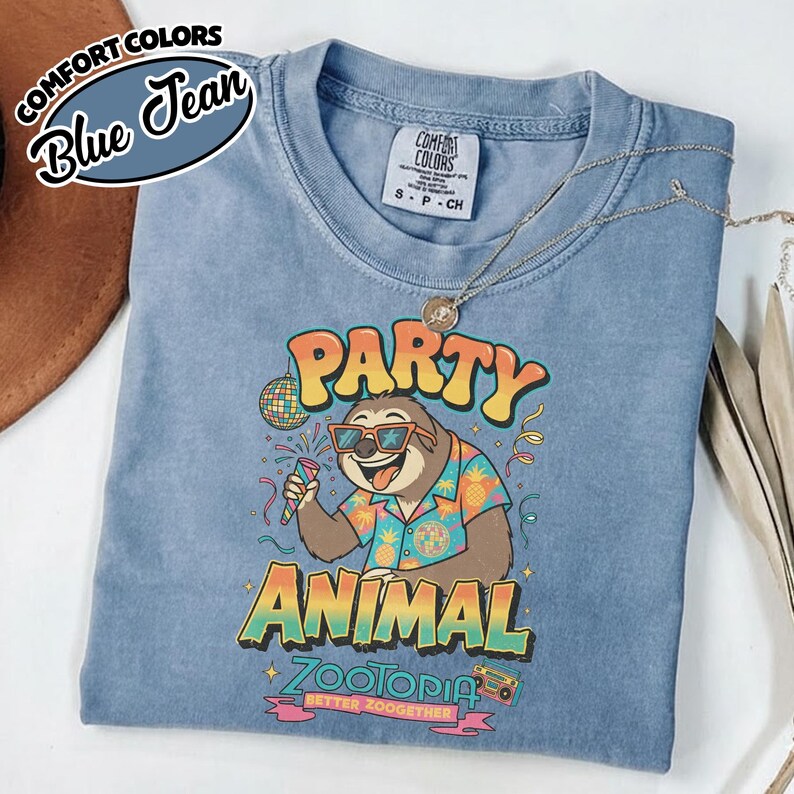 May include: Blue jean Comfort Colors t-shirt featuring a sloth wearing sunglasses and a Hawaiian shirt, holding a microphone. The shirt has the words "PARTY ANIMAL ZOOTOPIA" printed on it. A necklace is draped on the shirt.