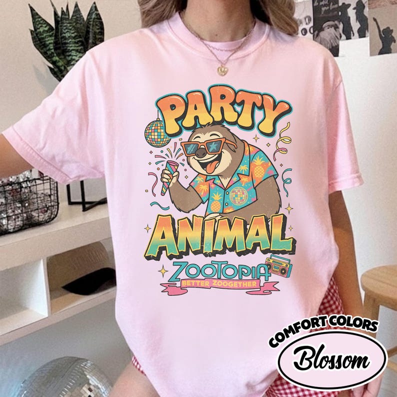 May include: Pink t-shirt with a colorful graphic featuring a sloth wearing sunglasses and a Hawaiian shirt, holding a microphone. The text reads "PARTY ANIMAL ZOOTOPIA BETTER ZOOGETHER". The shirt is from Comfort Colors, Blossom.