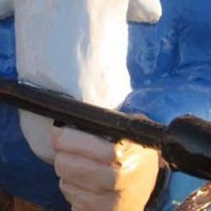 May include: A blue and white garden gnome holding a black torch with a yellow flame. The gnome is wearing a blue jacket and a white hat.
