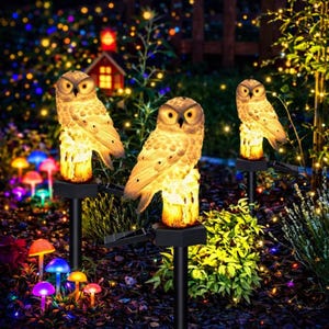 May include: Three solar-powered owl garden lights. The owl figurines are perched on faux tree stumps, with warm yellow light emanating from the base and eyes. The garden is illuminated with colorful mushroom lights and string lights, creating a whimsical outdoor scene.