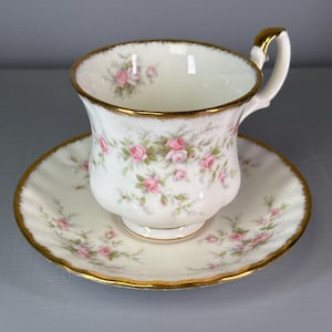 Può includere: Servizio da tè bianco con motivo floreale a rose. La tazza e il piattino hanno un bordo dorato. La tazza ha un manico e poggia su un piattino abbinato. Decorato con rose rosa e foglie verdi. Stoviglie decorative.