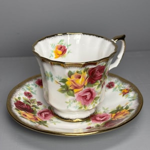 以下が含まれることがあります： 赤と黄色のバラ模様が施された、白のティーカップとソーサーのセット。縁は金でトリミングされています。ティーカップはスカラップの縁と金のハンドルが付いています。ソーサーは丸いです。