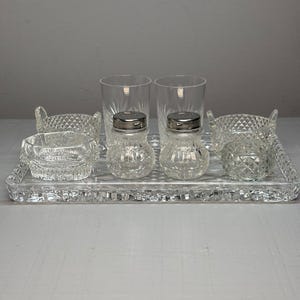 Peut inclure: Un ensemble de service en verre transparent comprenant un plateau rectangulaire à motif diamant, deux grands verres, deux petites salières et poivrières à couvercles métalliques argentés et quatre petits bols en verre taillé.