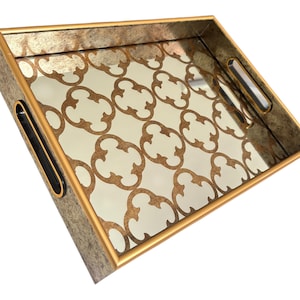 May include: Rectangular decorative tray with a mirrored surface featuring a gold quatrefoil pattern. The tray has a gold-coloured frame and handles with a textured, metallic finish. Ideal for serving or display.