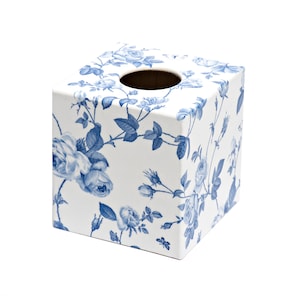 Puede incluir: Caja de pañuelos cuadrada con fondo blanco y un patrón floral azul. El diseño presenta rosas y follaje, creando un aspecto clásico y elegante. La parte superior tiene una abertura circular.