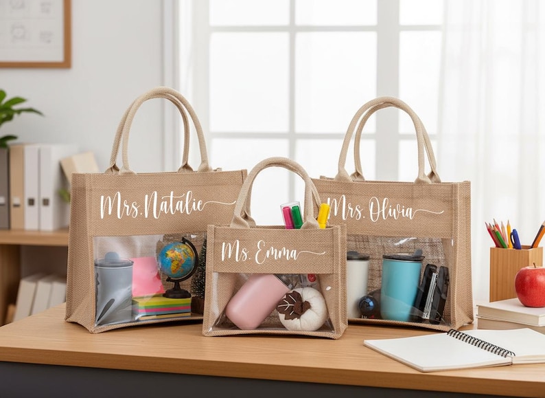 May include: Three tan burlap tote bags with clear plastic windows on the front. Each bag features white cursive text: Mrs. Natalie, Ms. Emma, and Mrs. Olivia. The bags have two top handles and are filled with various office and school supplies.