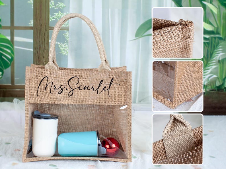 May include: A tan burlap tote bag with two beige handles and a clear plastic window on the front. The text Mrs. Scarlet is printed in black script on the upper burlap section. Inside the bag are a white tumbler, a light blue tumbler, and a red ornament.