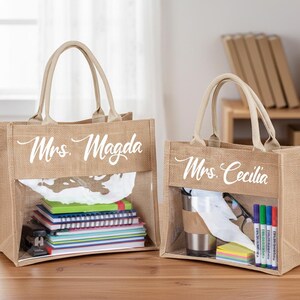 May include: Two rectangular tan jute tote bags with beige handles and a clear plastic window on the front. The larger bag features the white text Mrs. Magda, and the smaller bag features the white text Mrs. Cecilia, both in a cursive script font.