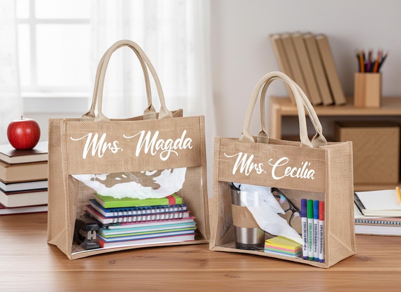 May include: Two rectangular tan jute tote bags with beige handles and a clear plastic window on the front. The larger bag features the white text Mrs. Magda, and the smaller bag features the white text Mrs. Cecilia, both in a cursive script font.