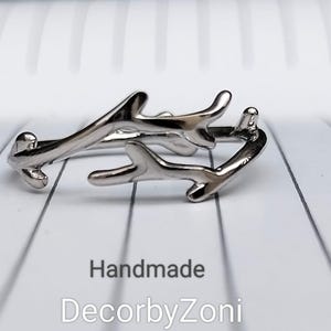 May include: A silver ring featuring a branch design. The ring has a distinctive, nature-inspired look. The word "Handmade" and the brand name "DecorbyZoni" are printed below the ring.