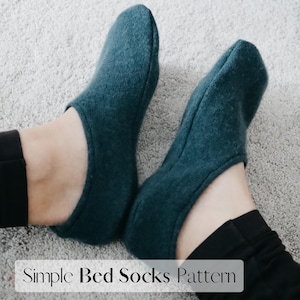 Op de afbeelding: Een paar teal bed sokken. De sokken zijn gemaakt van een zacht, viltachtig materiaal en hebben een open hiel ontwerp. De tekst "Simple Bed Socks Pattern" staat onderaan de afbeelding.