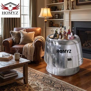 Puede incluir: Un enfriador de bebidas de metal pulido con la palabra "HOMYZ" en el lateral. El enfriador es cilíndrico con un diseño remachado y contiene varias botellas de vino y licor. Está colocado sobre un suelo de madera en un salón.