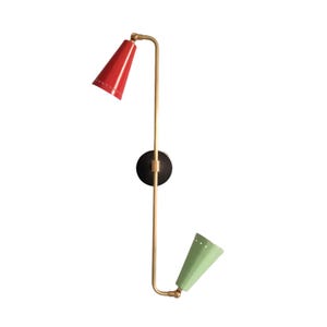 May include: A modern wall sconce with a red cone-shaped shade and a green cone-shaped shade. The fixture has a brass-colored arm and a black circular base. The light fixture is designed to be mounted on a wall.