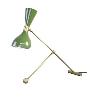 Puede incluir: Lámpara de escritorio verde y latón con brazo ajustable. La lámpara tiene una pantalla cónica y una base de latón. El brazo se extiende hasta una bola de latón y una base rectangular. La lámpara está diseñada para un escritorio o mesa. Medidas en centímetros.