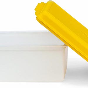 May include: A white rectangular food storage container with a yellow lid. The lid is slightly ajar, revealing the container's interior. The container is made of a translucent material, and the lid is a bright yellow.