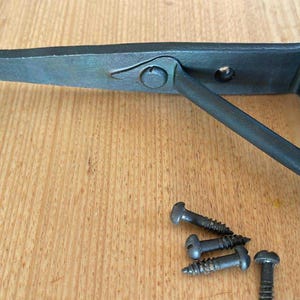 May include: A dark grey metal shelf bracket with a decorative design. The bracket has a curved end and a support arm. Several screws are included. Hardware for home decor.