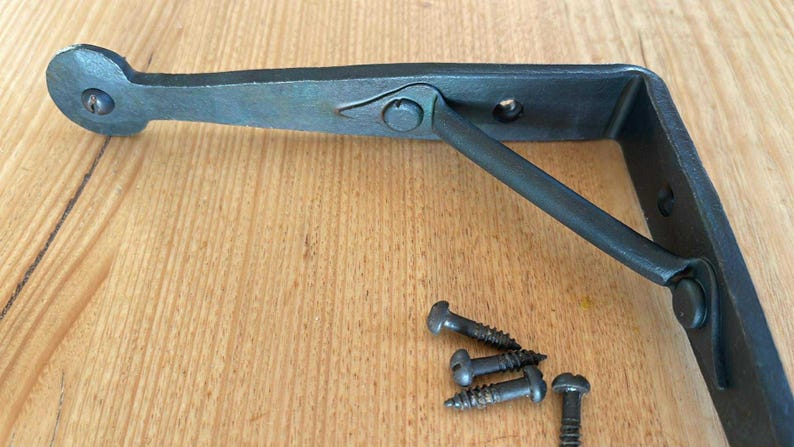 May include: A dark grey metal shelf bracket with a decorative design. The bracket has a curved end and a support arm. Several screws are included. Hardware for home decor.