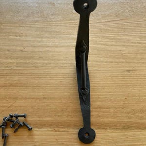 May include: Black wrought iron door pull with a curved handle and circular ends. Includes a set of screws for installation. The handle has a decorative, textured finish, suitable for rustic or farmhouse decor.
