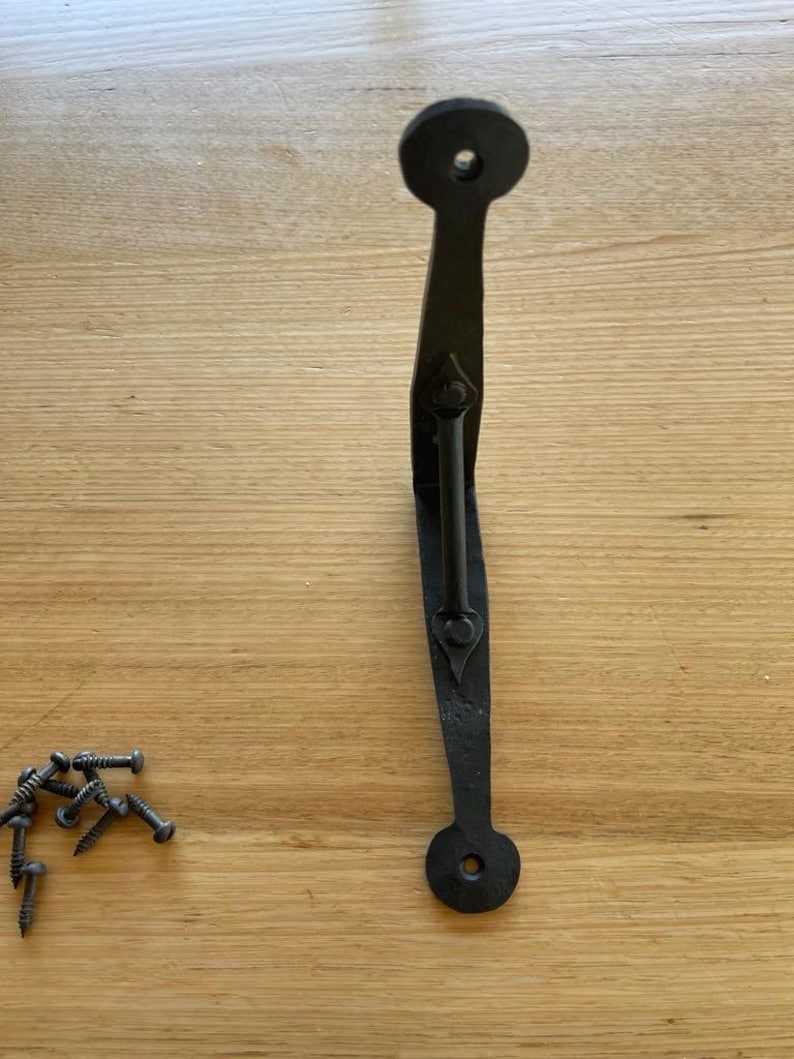 May include: Black wrought iron door pull with a curved handle and circular ends. Includes a set of screws for installation. The handle has a decorative, textured finish, suitable for rustic or farmhouse decor.