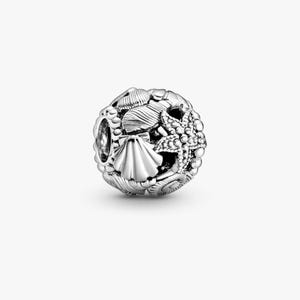 May include: A spherical silver charm bead featuring a detailed relief design of various seashells and a textured starfish. The surface of the bead is intricately carved with multiple types of shells, including a prominent fan-shaped scallop shell.