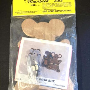 May include: A Mac-Wood Kits Teddy Bear Box craft set in a clear plastic bag with a yellow header card. The kit includes unfinished wooden bear-shaped pieces and an instruction sheet showing finished examples measuring 5 1/2 inches by 7 1/2 inches.