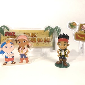 May include: Jake and the Never Land Pirates cake topper set featuring Jake, Izzy, and a treasure chest. The set includes a banner with the text "No Ho, Way To Go!"