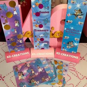 Könnte beinhalten: Drei vertikale rechteckige Spartracker und mehrere quadratische Karten mit Aladdin-Figuren, goldenen Lampen und Rubbelkreisen. Jeder Artikel ist mit KS-CREATIONS beschriftet und zeigt verschiedene Geldbeträge in britischen Pfund.