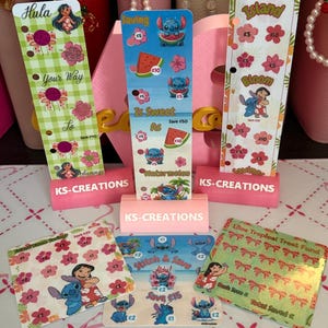 May include: Three vertical and three square laminated savings trackers featuring Lilo and Stitch characters, floral patterns, and watermelon graphics. Each tracker includes KS-CREATIONS branding, various monetary values in pounds, and designated spots for marking progress toward financial goals.