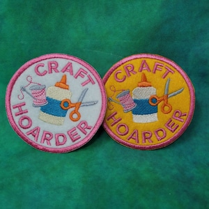 May include: Two embroidered patches with the text "CRAFT HOARDER". One patch is white with pink accents, the other is yellow with pink accents. Each patch features a glue bottle, scissors, and a spool of thread.