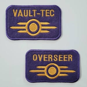 Pode incluir: Duas etiquetas retangulares roxas com texto bordado dourado e um emblema circular. A etiqueta superior diz "VAULT-TEC", e a etiqueta inferior diz "OVERSEER". O emblema apresenta um círculo com linhas horizontais em ambos os lados.