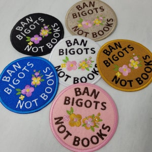 May include: Embroidered patches in black, white, blue, beige, gold, and pink. Each patch displays the text "BAN BIGOTS NOT BOOKS" in a circular design. Floral embellishments in pink, yellow, and green are also present on each patch.