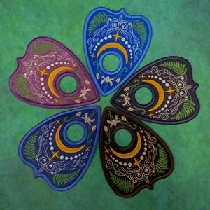 May include: Five embroidered planchette patches arranged in a circle. Each patch features a central circular cutout, a yellow crescent moon, white stars, and green fern leaf embroidery. The patches are purple, blue, dark blue, black, and brown.