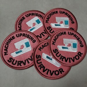 May include: A cluster of circular embroidered patches. Each patch is a dusty rose colour, featuring the words "MACHINE UPRISING" and "SURVIVOR" in black. A white sewing machine with teal accents is in the centre.