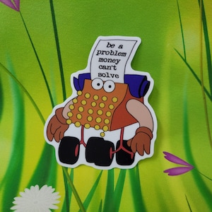 Pode incluir: Um autocolante com um personagem de máquina de escrever de desenho animado com um corpo castanho, teclas laranja e rodas pretas grandes. A máquina de escrever tem um pergaminho na cabeça e o texto "be a problem money can't solve".