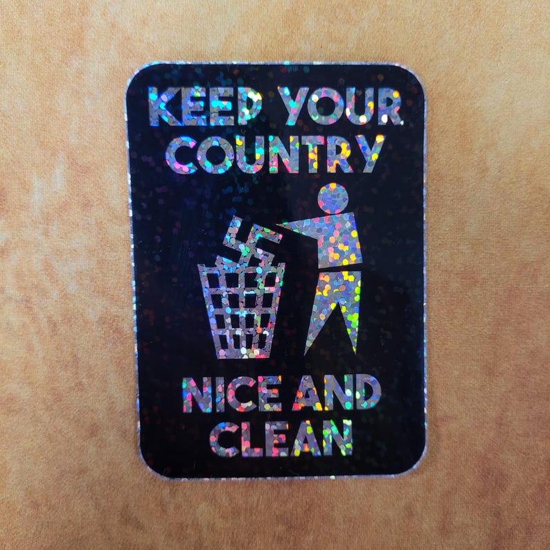 May include: A rectangular sticker with a black background and holographic glitter effect. The sticker features the text "KEEP YOUR COUNTRY NICE AND CLEAN" above an illustration of a person throwing a symbol into a trash can.