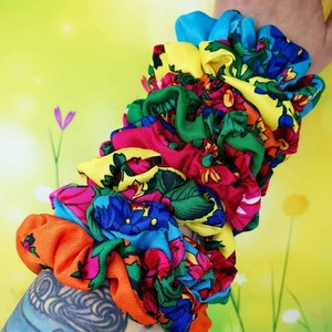 Può includere: Una collezione di elastici colorati con vari motivi floreali. Gli elastici presentano tonalità vivaci di blu, giallo, rosso, verde e arancione. Questi accessori per capelli sono realizzati in tessuto e sono raccolti per creare un aspetto voluminoso.