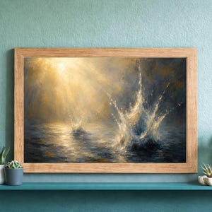 May include: A framed art print showing a water splash. The painting captures a splash of water in the center, with light reflecting on the water's surface. The color scheme includes blues, golds, and whites. The frame is made of light-coloured wood.
