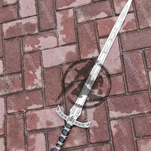 May include: A silver and black sword with a decorative hilt and a red gem at the pommel. The blade has a detailed design. The sword is lying on a brick surface. The text "Highland Blades" is visible.