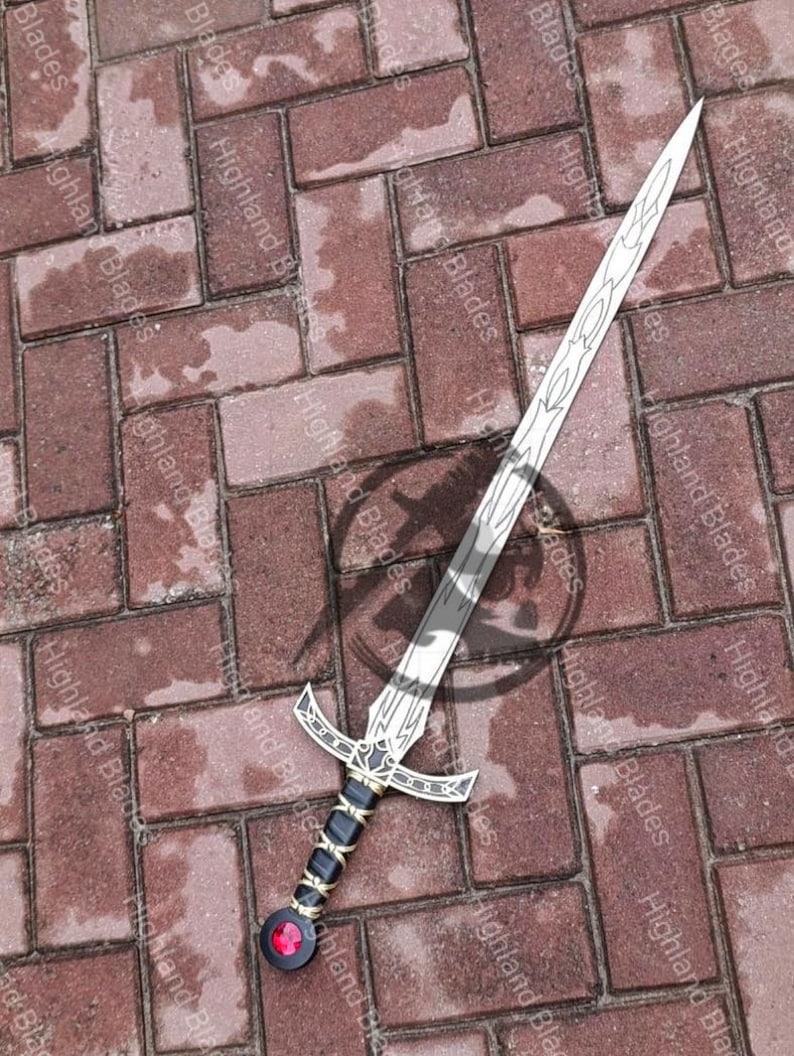 May include: A silver and black sword with a decorative hilt and a red gem at the pommel. The blade has a detailed design. The sword is lying on a brick surface. The text "Highland Blades" is visible.