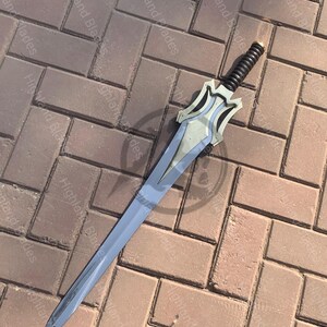 May include: A silver and blue sword with a black handle. The blade is long and slender, with a pointed tip. The hilt features a decorative design. The sword is lying on a brick surface.