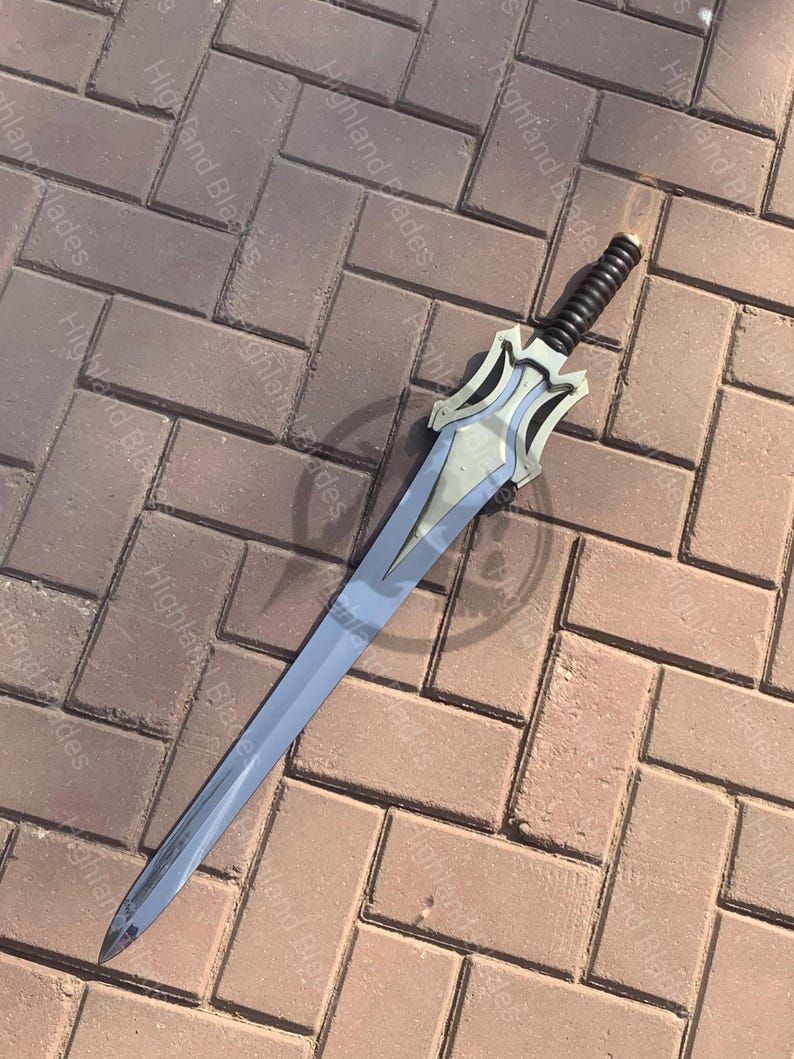 May include: A silver and blue sword with a black handle. The blade is long and slender, with a pointed tip. The hilt features a decorative design. The sword is lying on a brick surface.