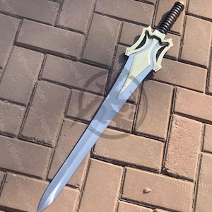 May include: A silver-colored sword with a decorative hilt and a black handle. The blade is long and slender, with a pointed tip. The hilt has a stylized design with a light gold color. The sword is lying on a brick surface.