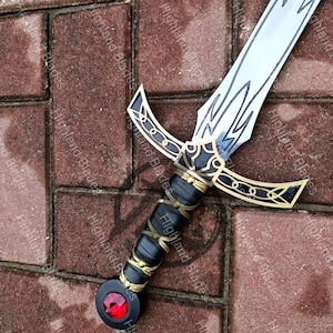 May include: A decorative sword with a silver blade and ornate black and gold hilt. The hilt features a black grip with gold accents and a red gem at the pommel. The sword is displayed on a brick surface.