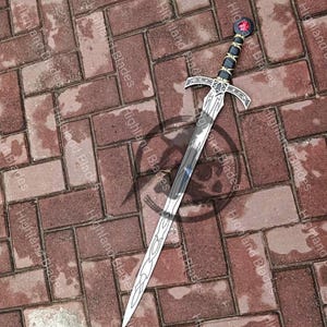 May include: A silver sword with a decorative handle featuring black and gold accents and a red gem. The blade has an intricate design and is set against a brick background.