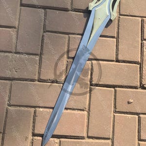 May include: A silver and gray sword with a decorative hilt and a black handle. The blade is long and pointed, and the hilt has a unique design. The sword is set against a brick background.