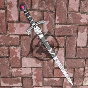 May include: A silver sword with a decorative hilt and a red gem at the pommel. The handle is black and gold, and the blade has an etched design. The sword is lying on a brick surface.
