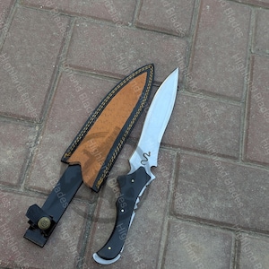 May include: A white ceramic mug with a black handle and the text "But First, Coffee" in a black, handwritten-style font. The mug is on a white surface.