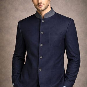 Puede incluir: Traje azul marino con cuello mao y detalle gris. La chaqueta tiene botones, dos bolsillos y un corte entallado. El traje se lleva con una camisa azul claro. Un estilo clásico y elegante.